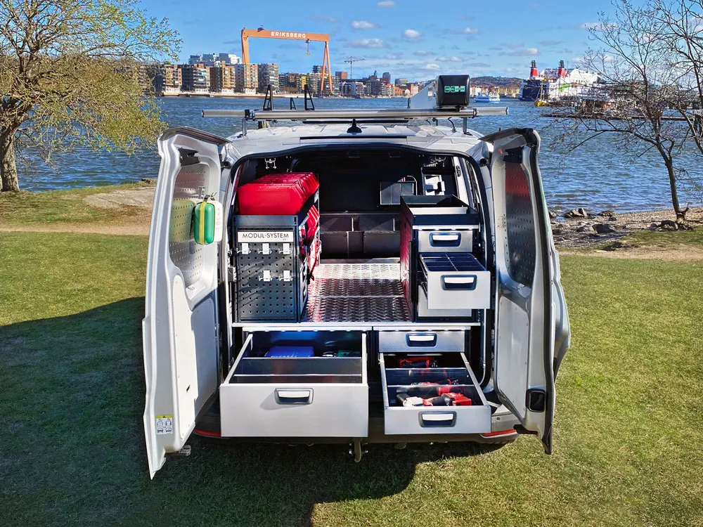 Rear view of a van with open doors showing a racking system with drawers, shelves and storage boxes